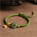 Close-up of a women's hand-woven green rope bracelet with a Hetian jade peace buckle charm.