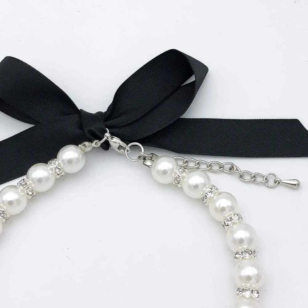 Small dog wearing adjustable pearl and rhinestone necklace with ribbon bow collar
