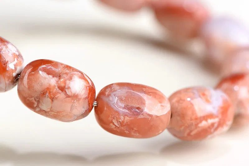 Natural cherry agate bracelet with barrel-shaped beads and a gold Ruyi charm on an adjustable strap.