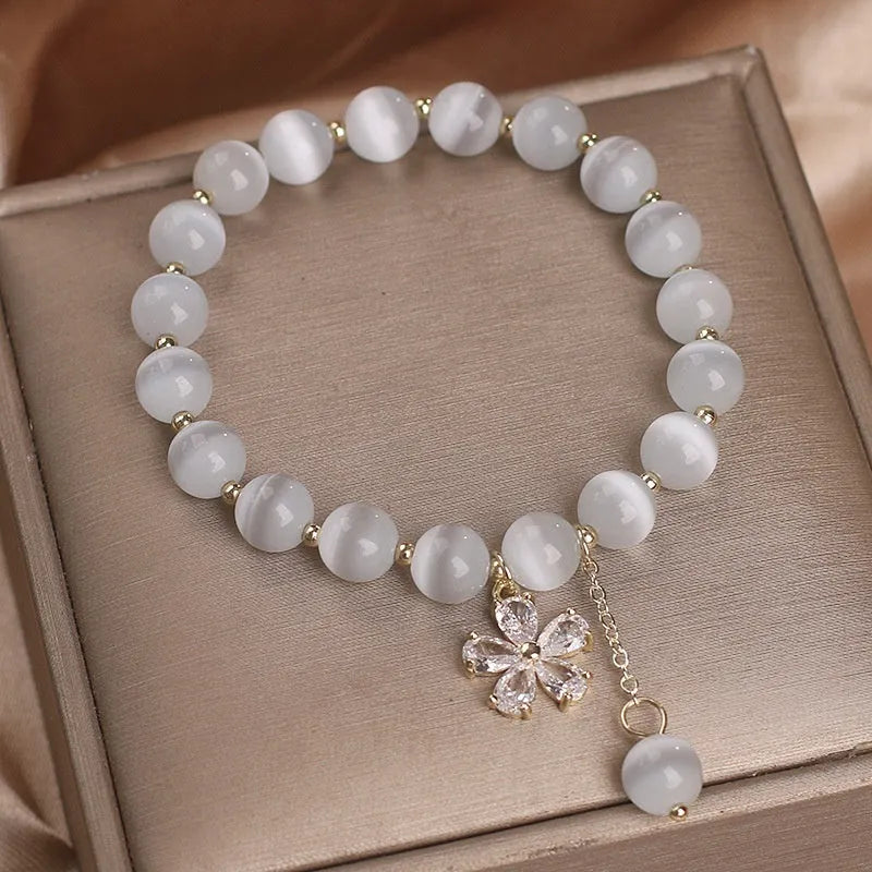 Close-up of a women's single loop bracelet with a white cat's eye stone, flower tassel, and pink morganite safety buckle pendant.