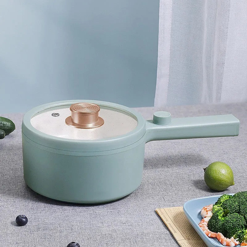 White and green multi-function electric cooking pot with temperature control dial, shown with a UK plug converter.