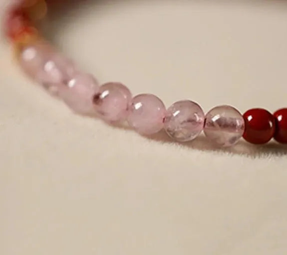 Hand-woven purple gold sand and strawberry quartz koi bracelet with crystal and pearl beads on a light background.
