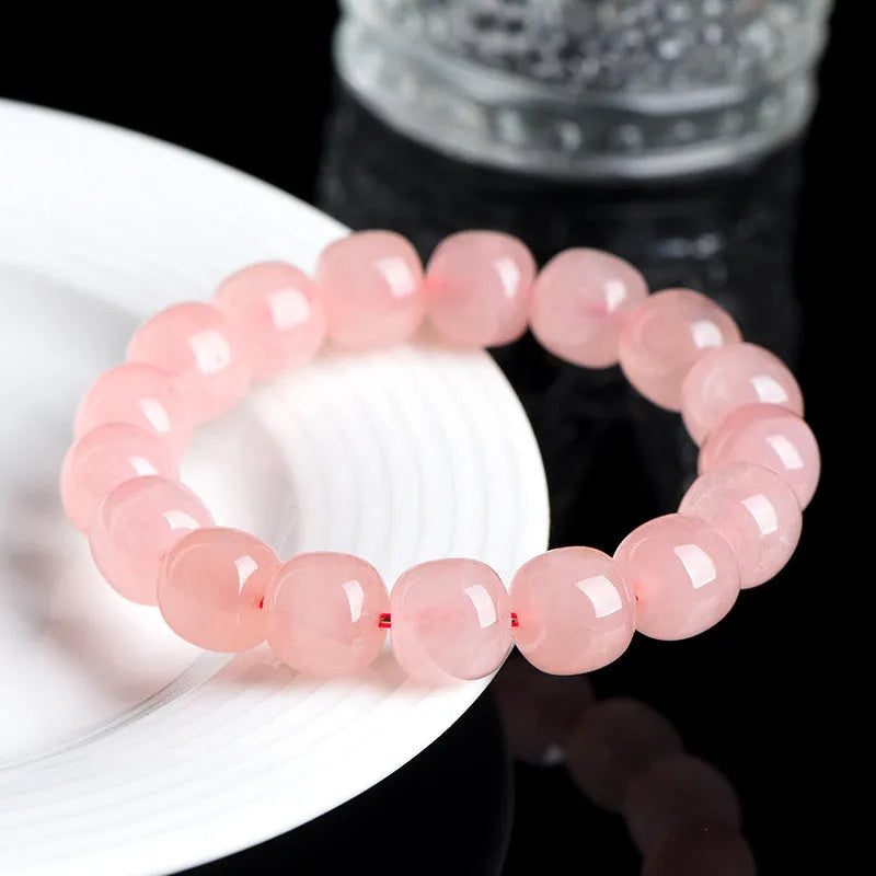 Close-up of a pink natural crystal barrel bead bracelet with geometric shaped beads on a wrist.