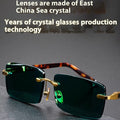 Dark green frameless crystal sunglasses with a hard case and cleaning cloth on a plain background.
