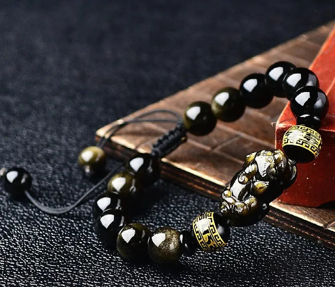 Hand-woven golden obsidian Pi Xiu bracelet with animal zodiac charm on wrist.
