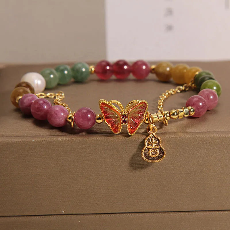 Close-up of an agate butterfly bracelet with a tourmaline-coloured gourd charm on a model's wrist.