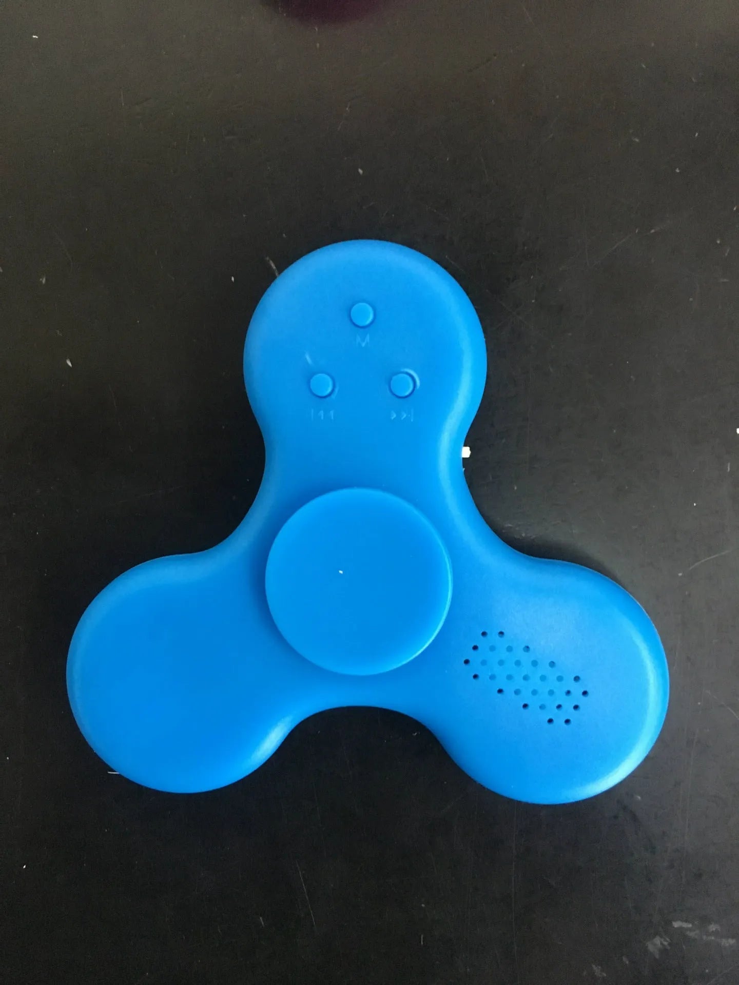 A square blue Bluetooth speaker and MP3 player with an integrated fidget spinner, showing button controls.