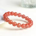 A close-up of a polished cherry red agate bead bracelet on a wrist.