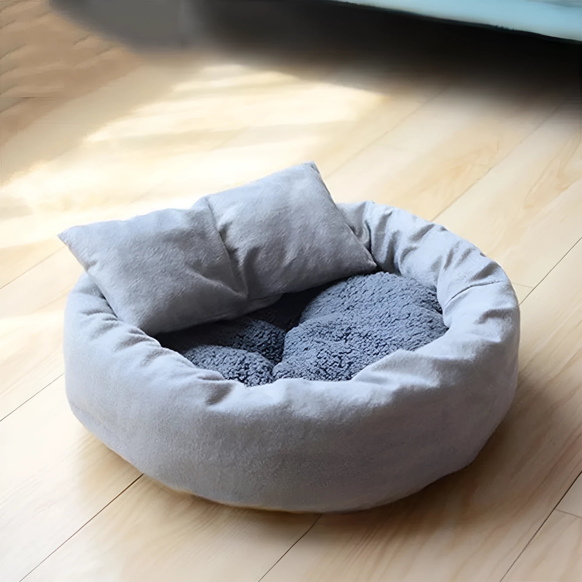 Grey round plush pet bed with pillow for small dogs and cats on a wood floor.